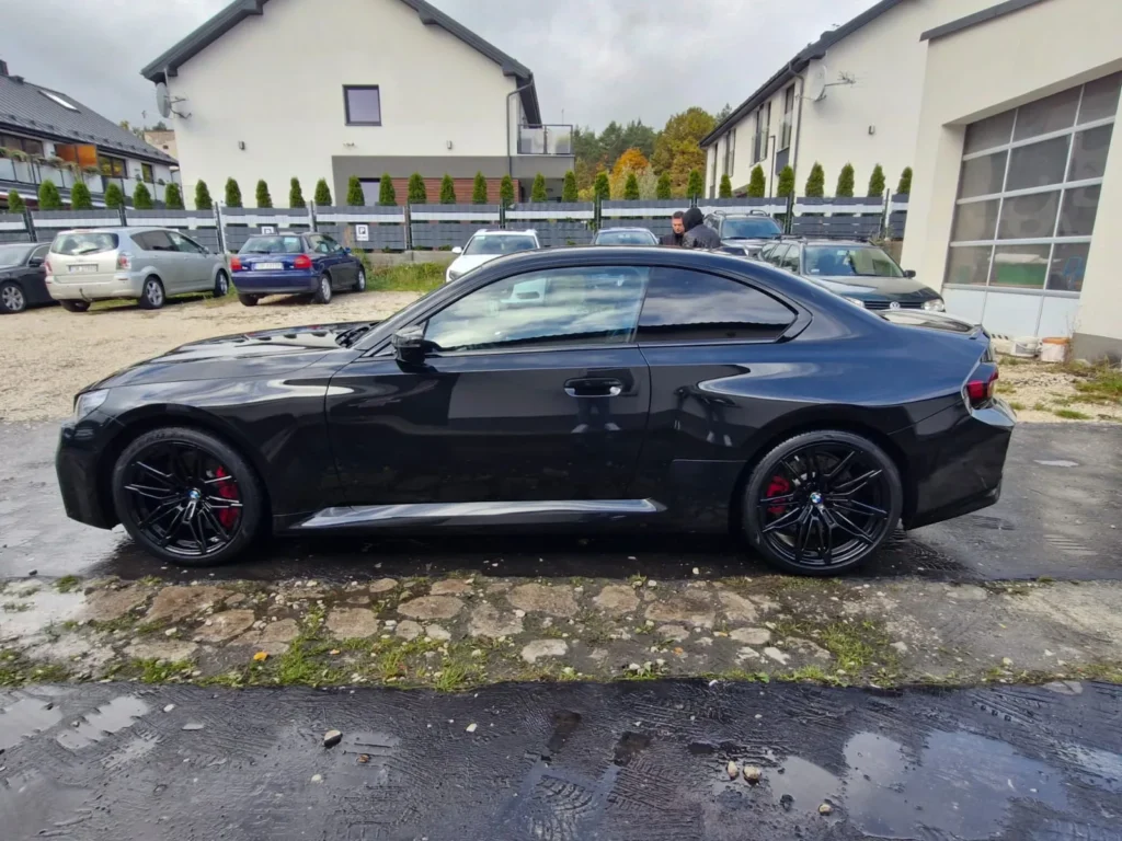 BMW M2 2024 czarne – widok z boku, sportowy samochód coupe na czarnych felgach, oferta wynajmu APKARS